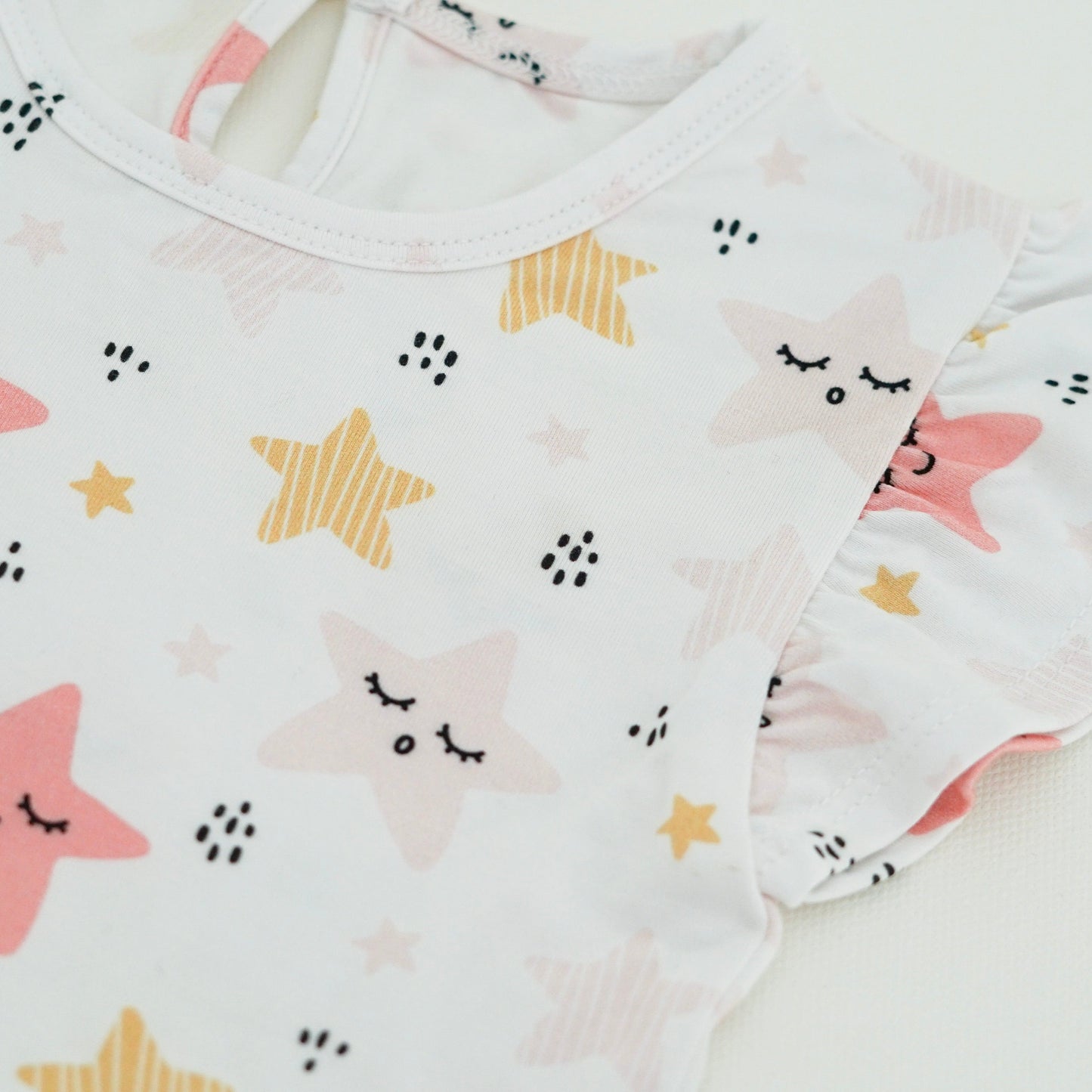 Close-up of a baby girl’s dress featuring a whimsical print of smiling pink and yellow stars, made from soft organic cotton by Issy & Lilo.