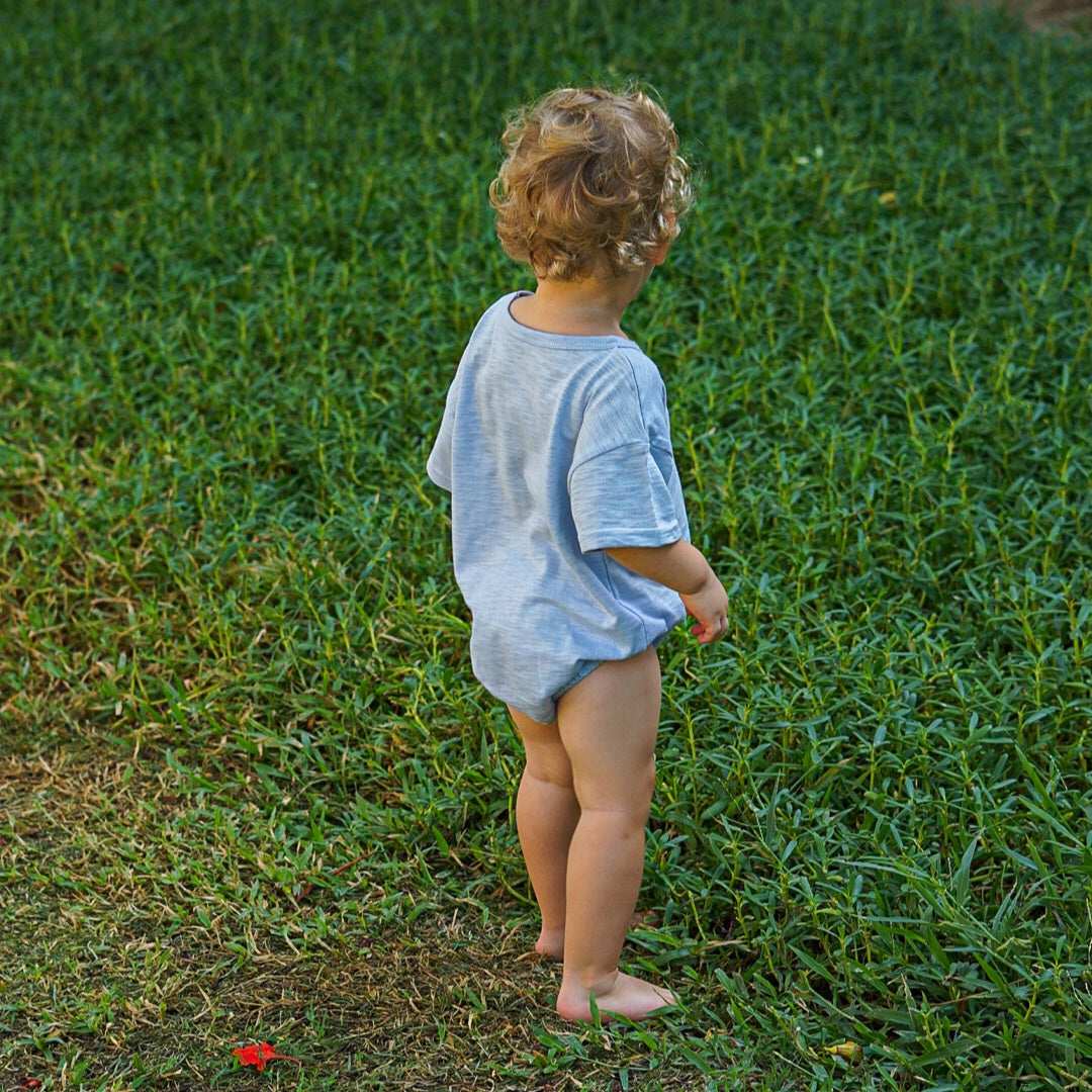 Toddler standing barefoot on grass, wearing an Issy & Lilo light blue organic cotton bodysuit