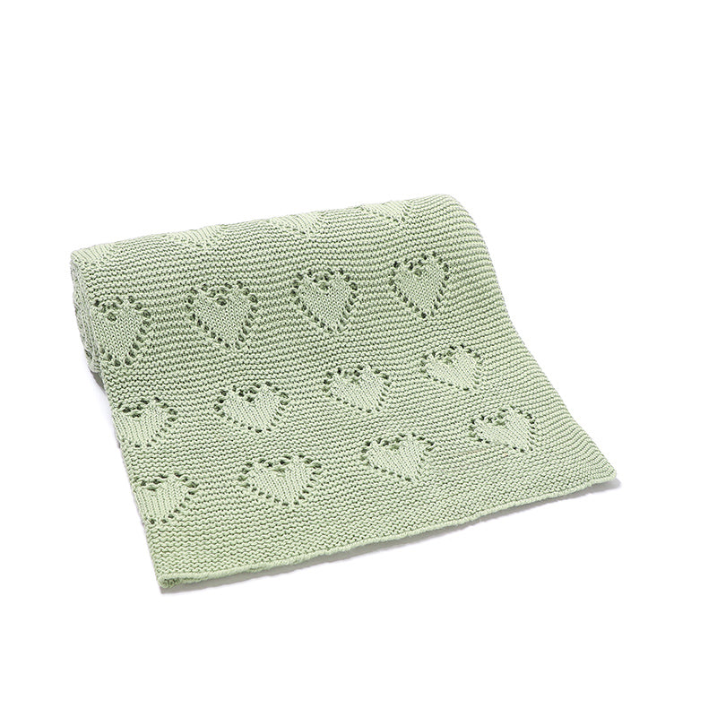 Issy & Lilo organic cotton blanket in green, partially unrolled, showcasing a heart-knit design