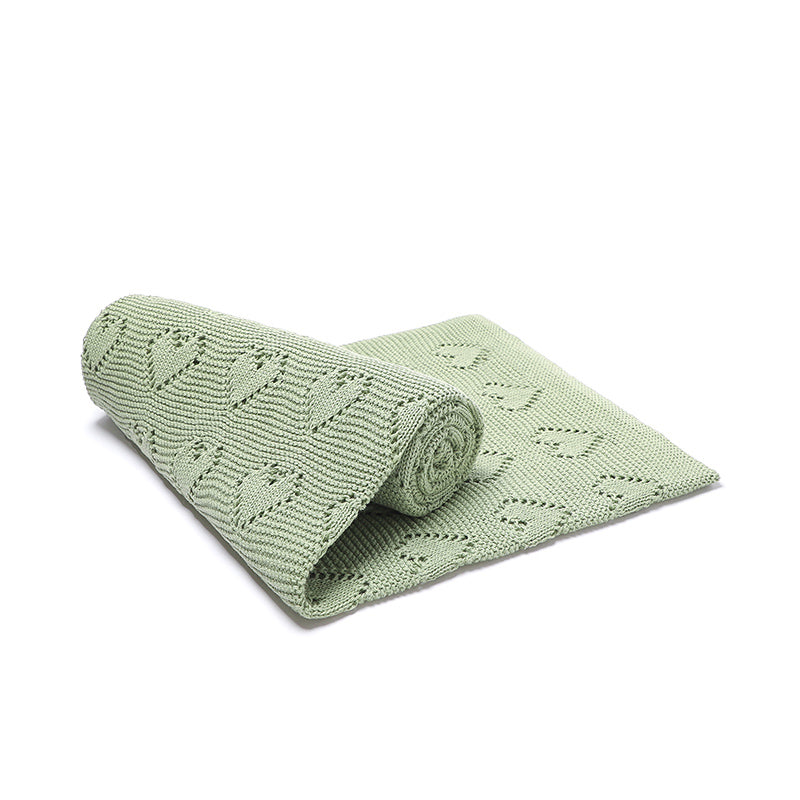 Issy & Lilo organic cotton blanket in green, rolled partially, showcasing heart-knit detailing