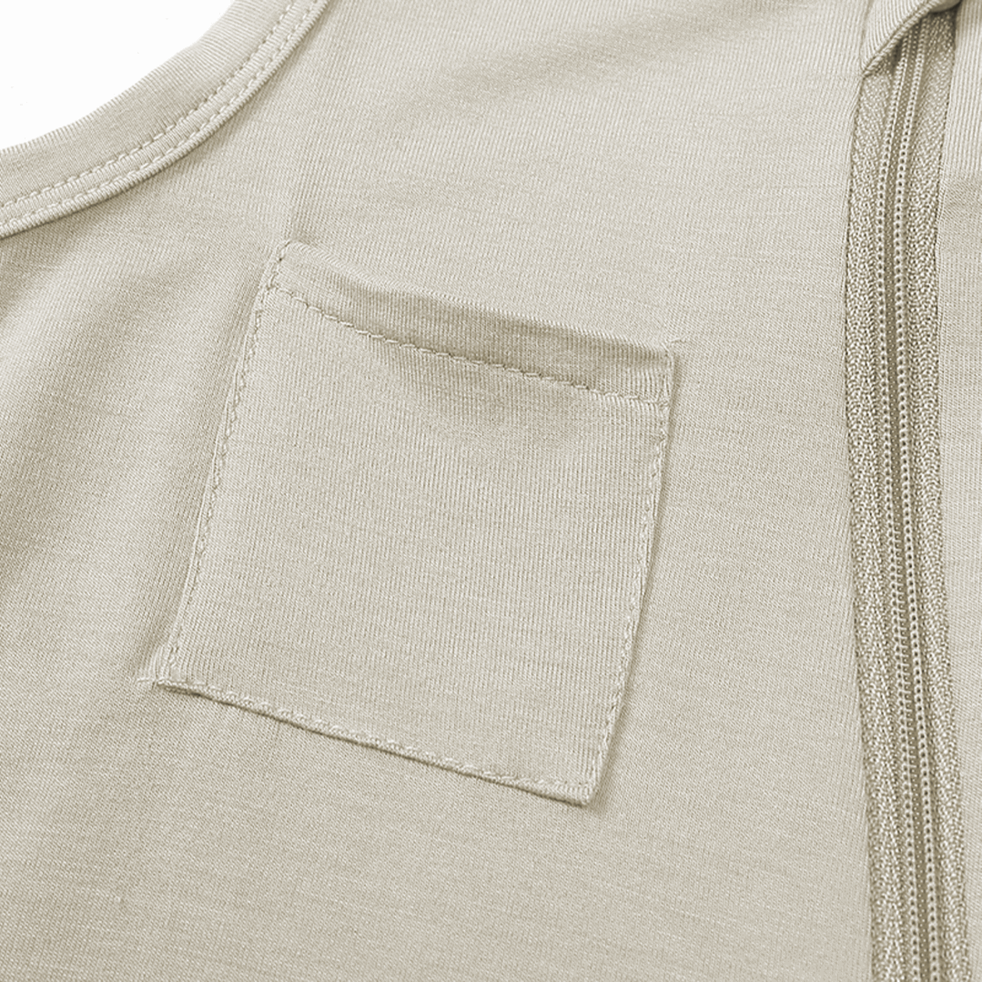 close-up of a small front pocket on cream-colored sleeveless bamboo baby overalls