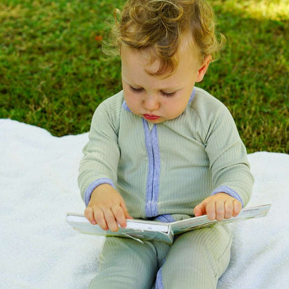 Toddler sitting on a white blanket outdoors, wearing a smart organic cotton zipper romper in sage green, holding a toy.