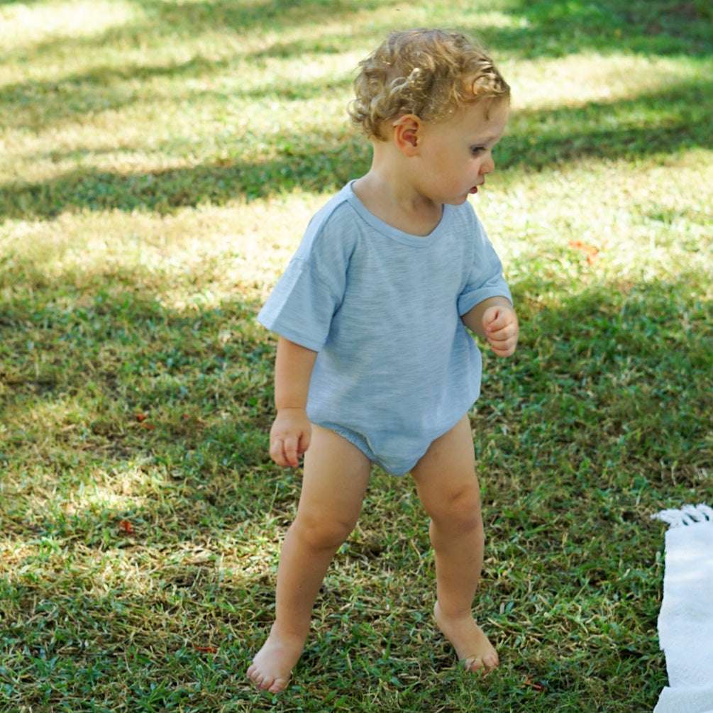 Toddler playing outdoors on grass, wearing an Issy & Lilo light blue organic cotton bodysuit