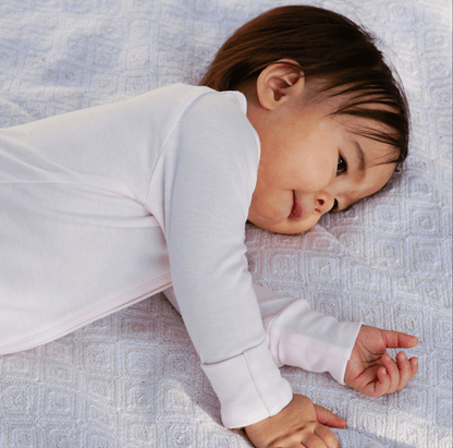 Baby lying down in a light pink bamboo onesie, resting on a soft white blanket, ideal for cozy sleep time.