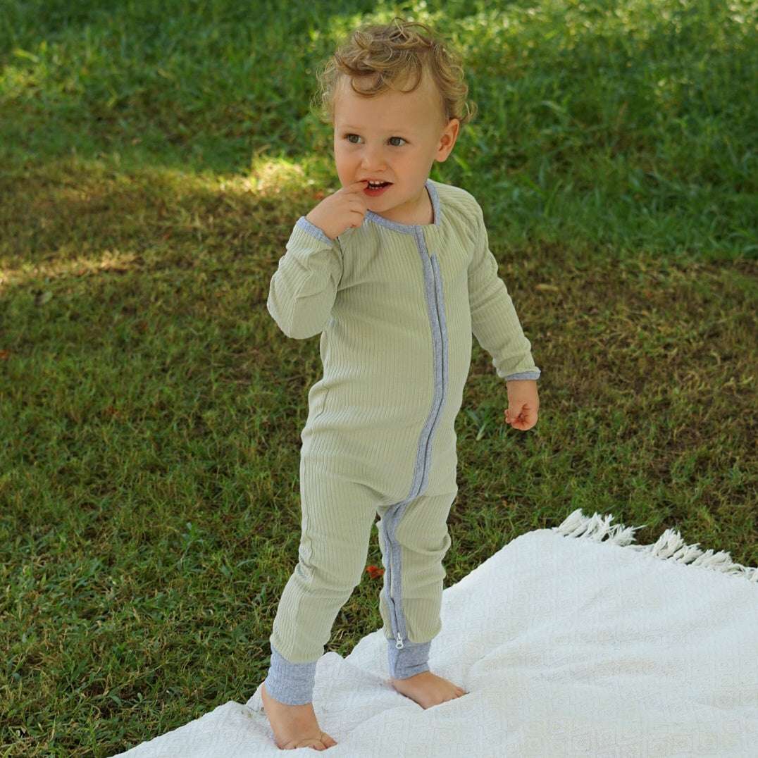 Toddler wearing a smart organic cotton zipper romper in sage green, standing outdoors on a white blanket.