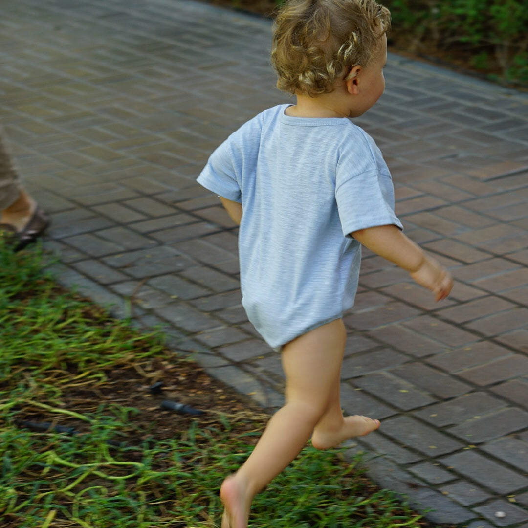 Toddler running barefoot on a paved path, wearing an Issy & Lilo light blue organic cotton t-shirt