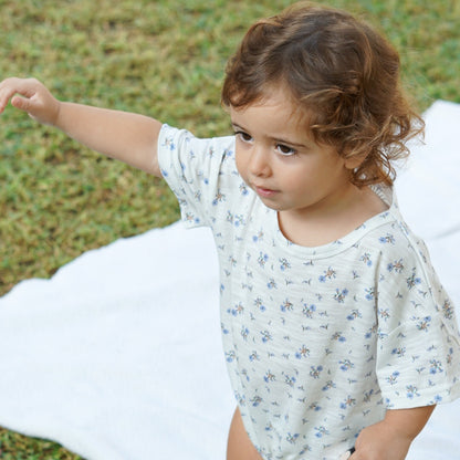 Toddler wearing an Issy & Lilo white organic cotton bodysuit with blue heart print, standing outdoors on a white blanket